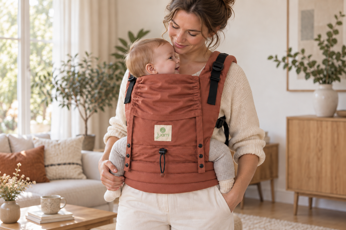 Moeder kijkt naar haar baby in een terracotta draagzak, thuis in de woonkamer.