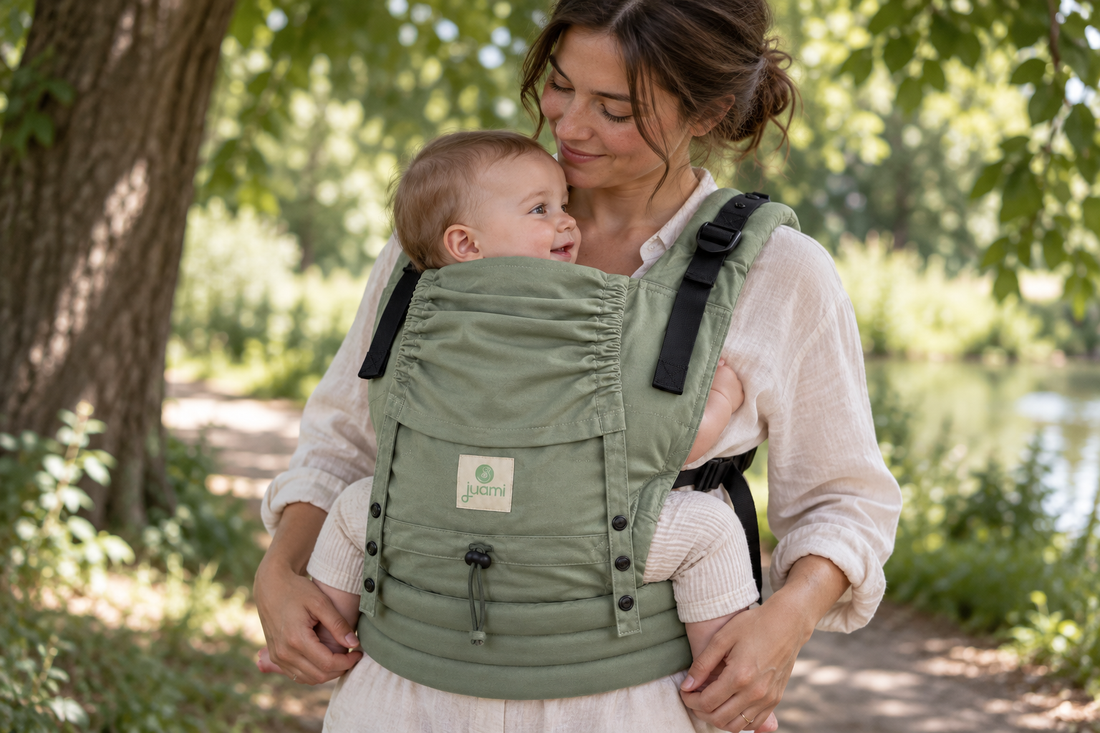 Ouder draagt een baby in een lichtgroene draagzak in de schaduw van bomen op een zomerdag.