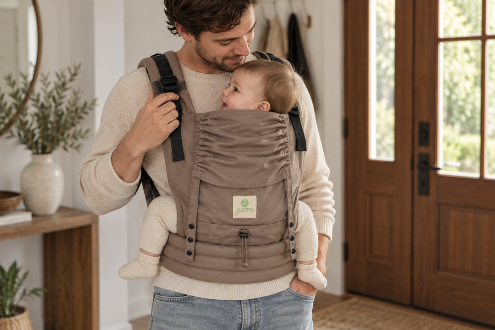 Vader controleert de schouderband van een taupekleurige draagzak voordat hij met zijn baby naar buiten gaat.