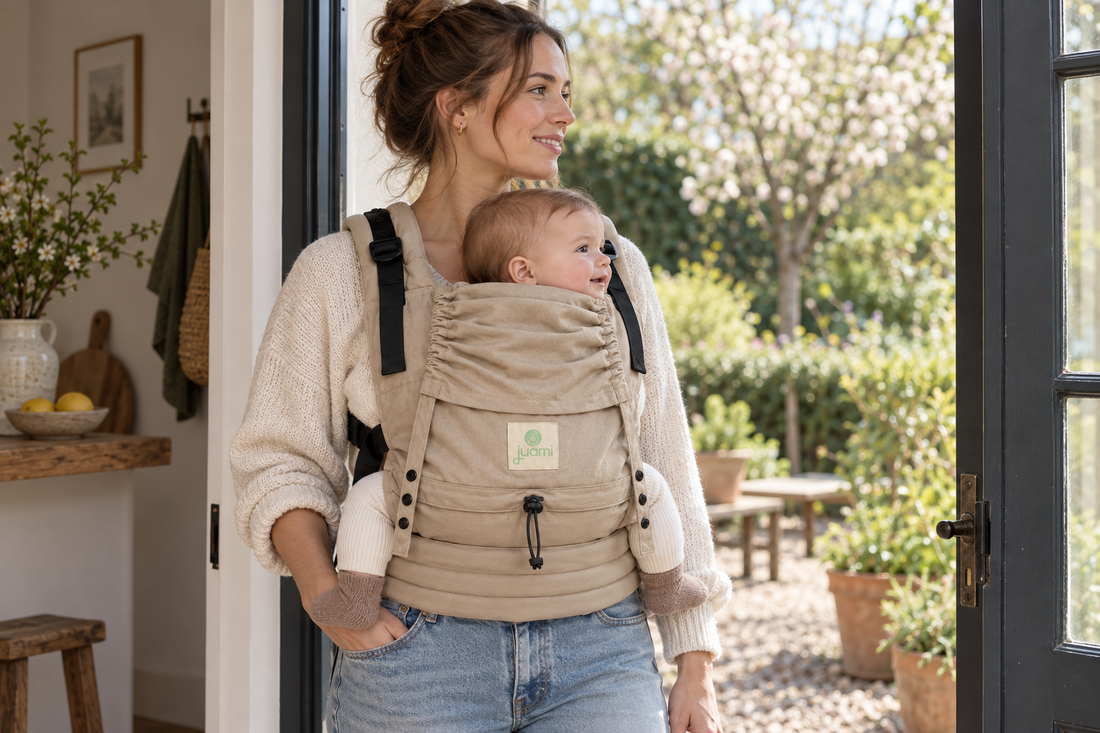 Moeder staat met haar baby in een zandkleurige draagzak bij de open deur naar de tuin.
