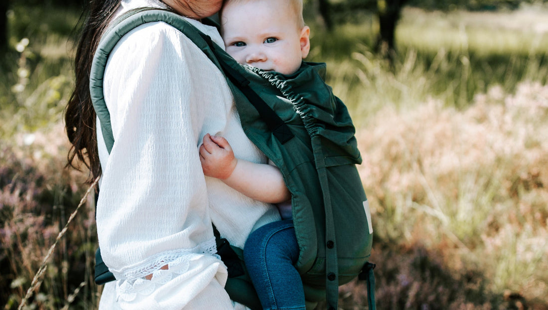 Moeder draagt haar baby op de buik in een ergonomische Juami draagzak, omringd door groene natuur in het bos.